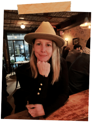 alyssa dineen owner of style my profile NYC sitting in resturant table with hat and black long sleeve shirt smiling at camera